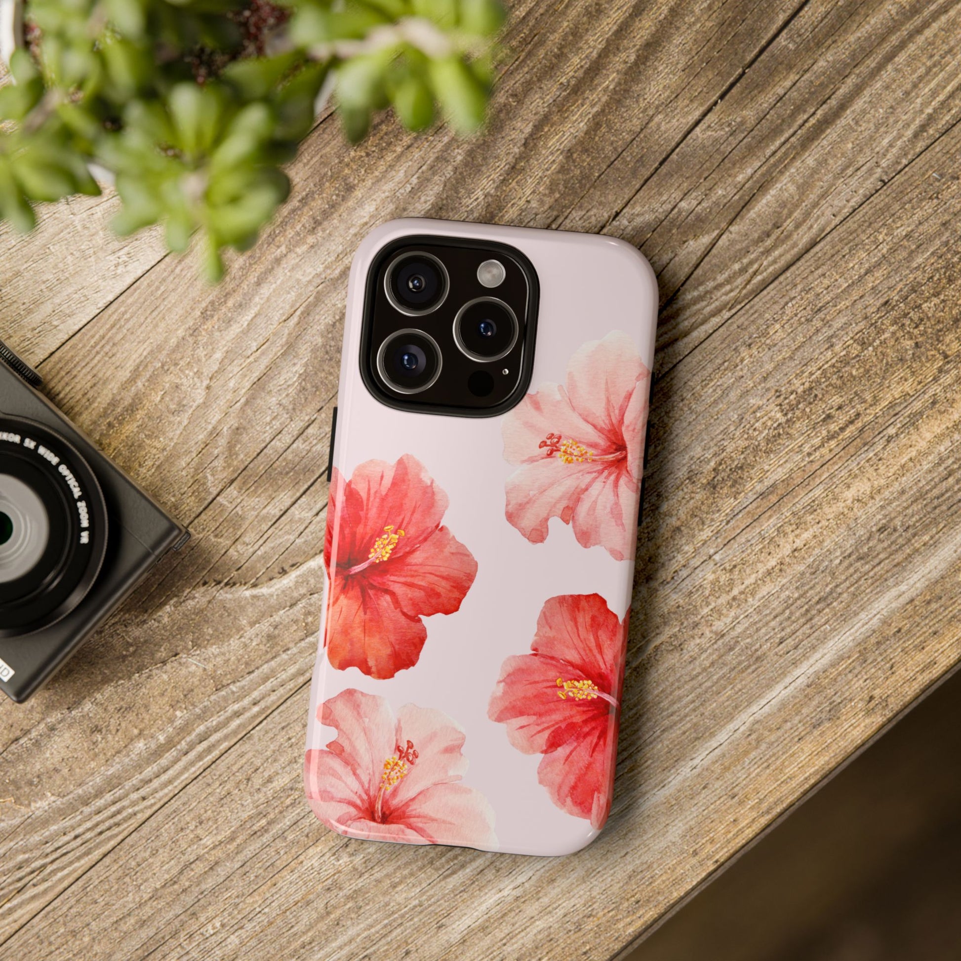 Phone case with floral design on a wooden surface next to a camera