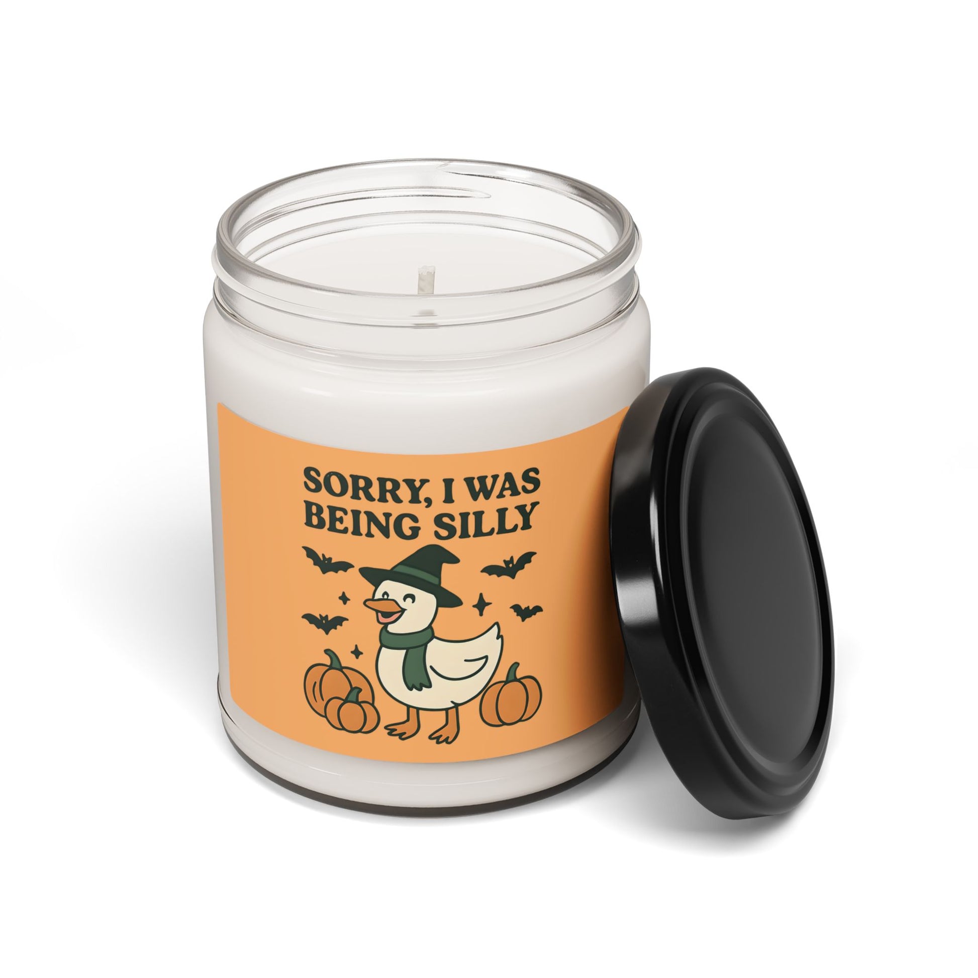 Candle jar with a Halloween-themed label featuring a duck in a witch hat and text 'Sorry, I was being silly' on an orange background.